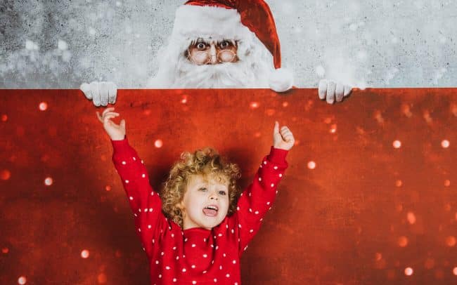 blond gelocktes Kind im Weihnachtspullover freut sich auf Weihnachten