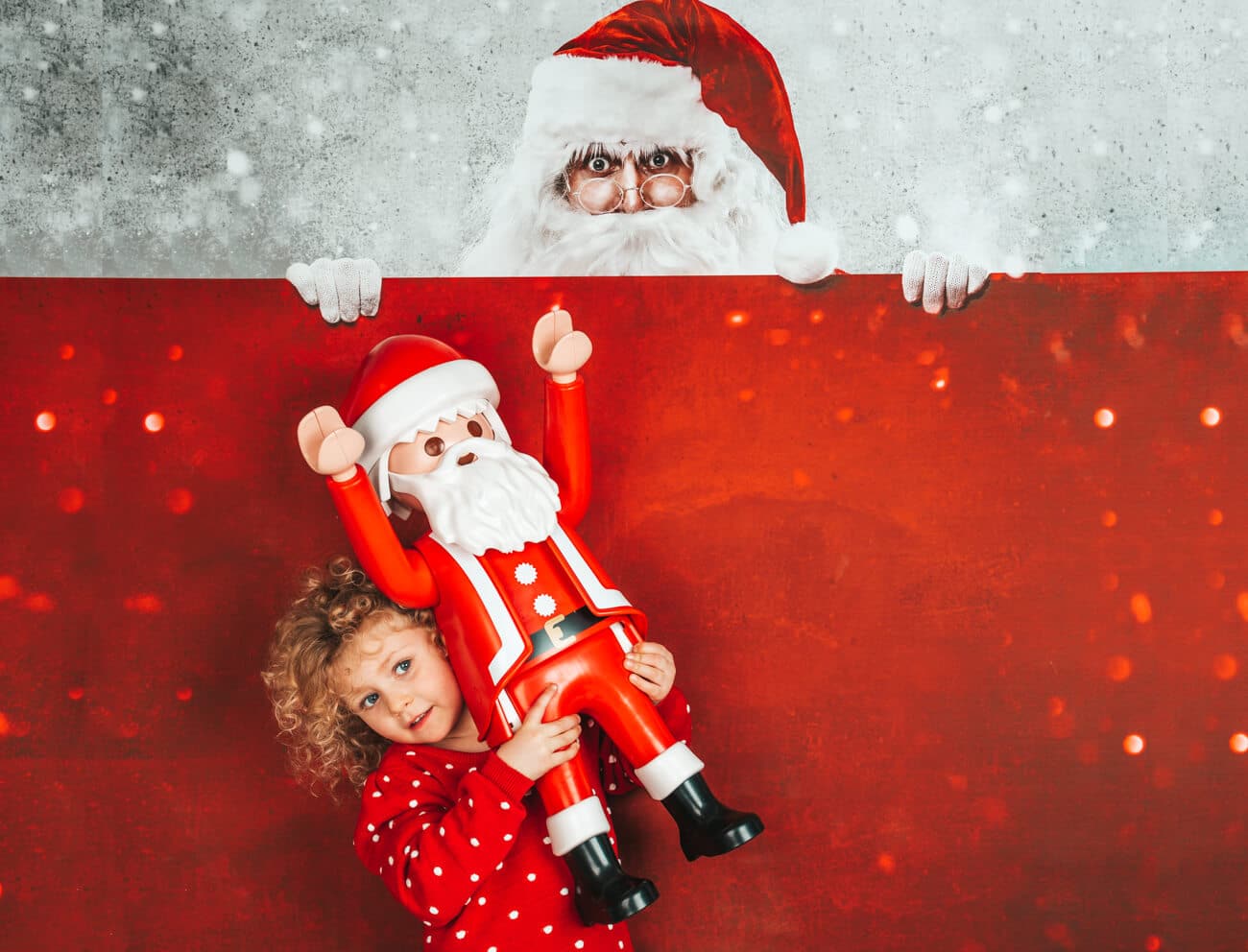 blond gelocktes Kind im Weihnachtspullover hebt Playmobil Weihnachtsmann hoch