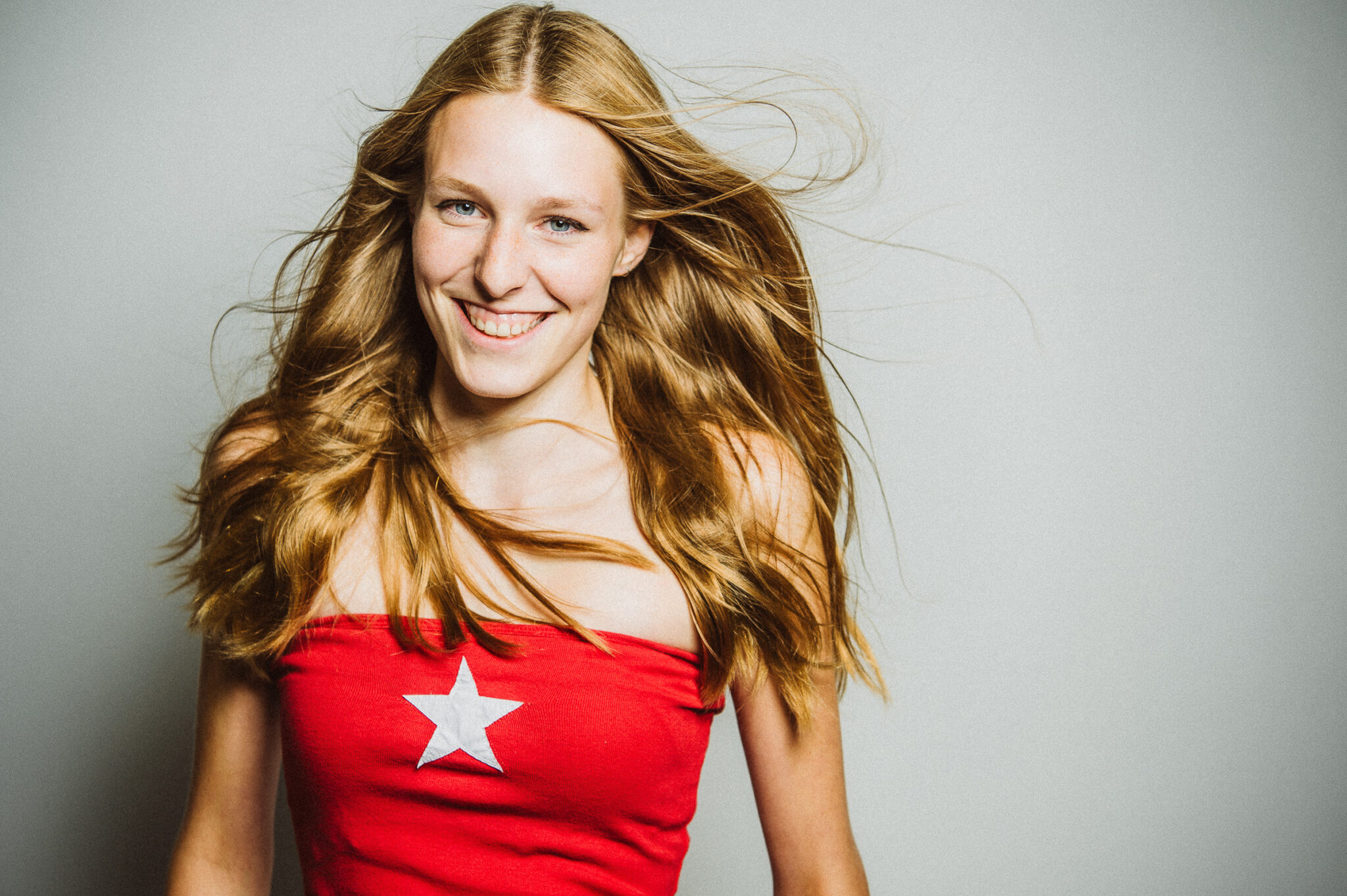 Portraitfotografie – Fashionfotografie by Miriam Merkel Lachende junge Frau im schulterfreien roten Top mit Stern Aufdruck